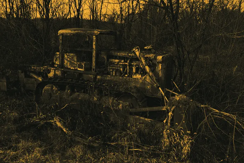 An abandoned yellow crawler tractor, rusted through, among bare winter brush