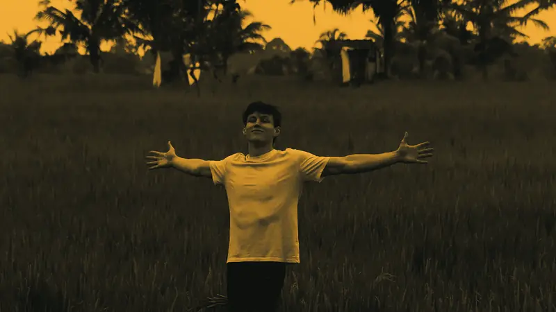 Jon Law with both arms outstretched among green rice plants, palm trees behind