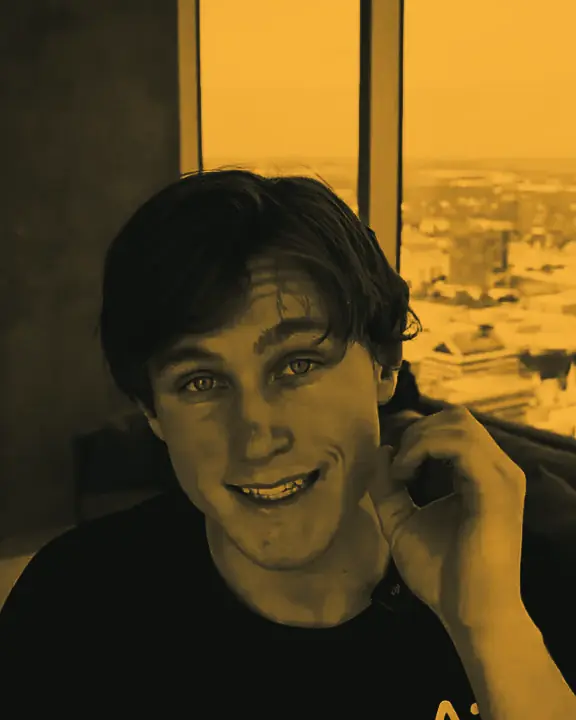 Jon Law talking to the camera with a city skyline in the window behind him
